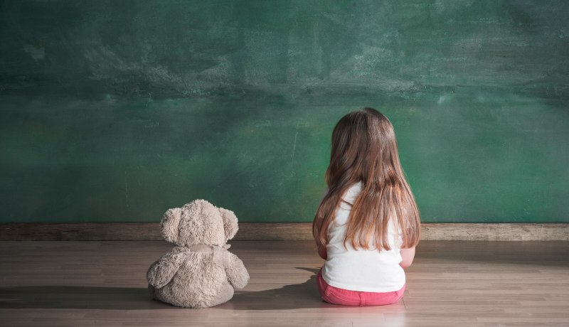 Overburdened and lonely only child myths busted! Little girl sitting with teddy bear, facing away